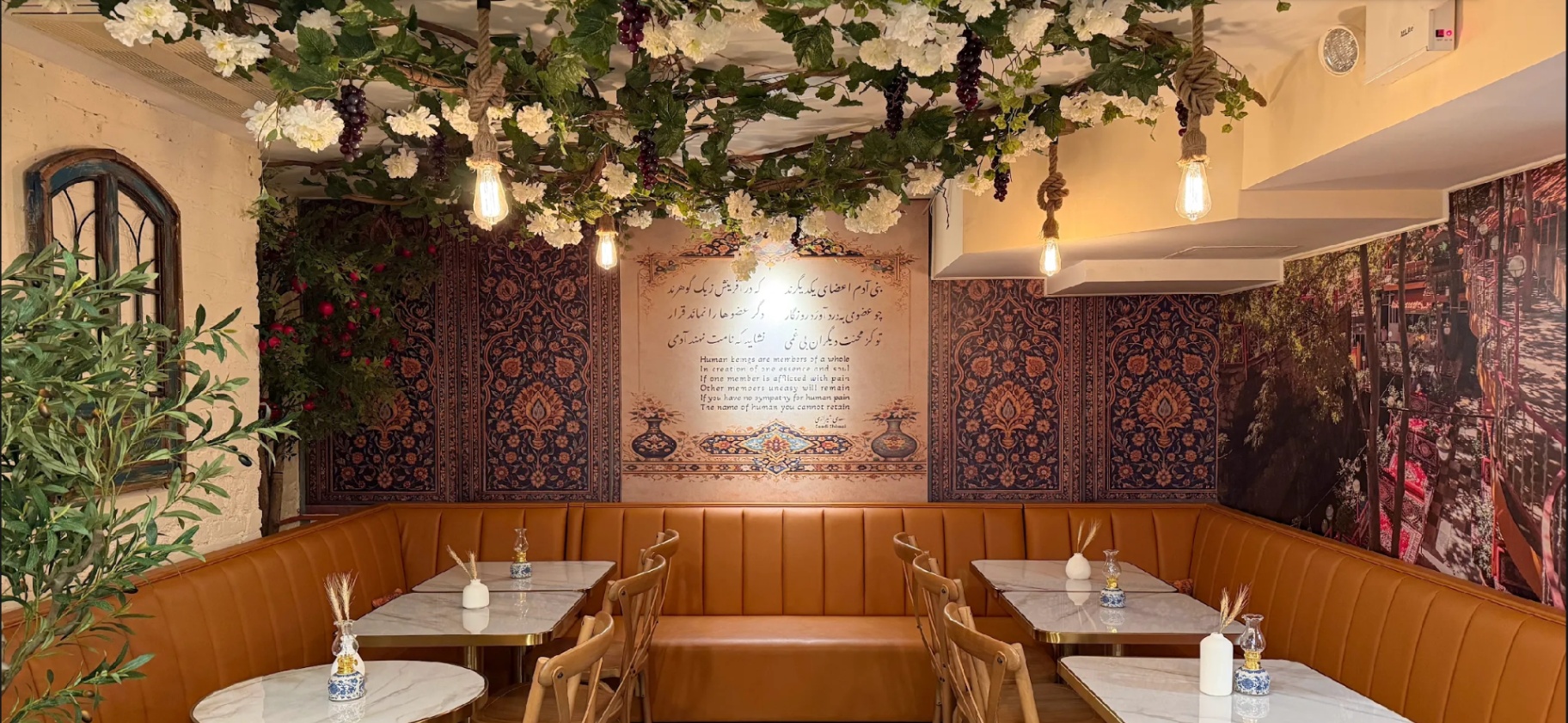 Blossoming canopy above cognac banquettes at Taftoon NYC with Saadi's Bani Adam poetry on the wall